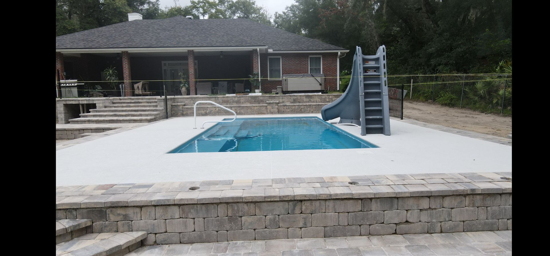 A large swimming pool with a slide in front of a house.