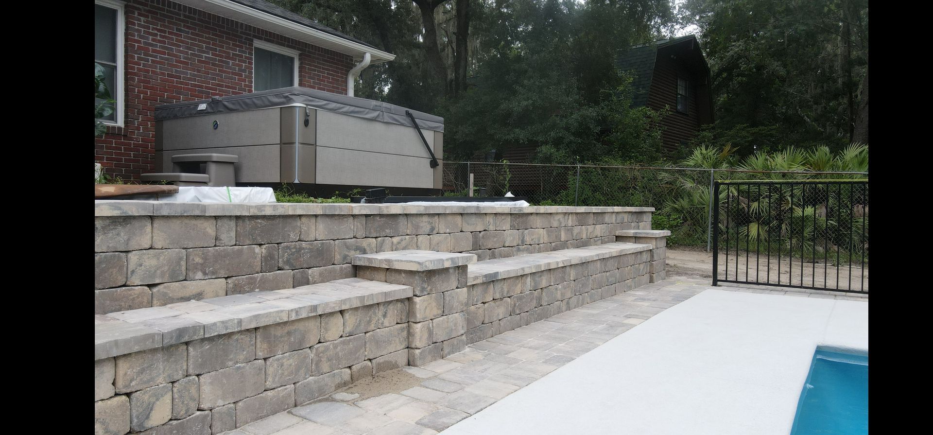 A hot tub is sitting on top of a paver wall next to a swimming pool.