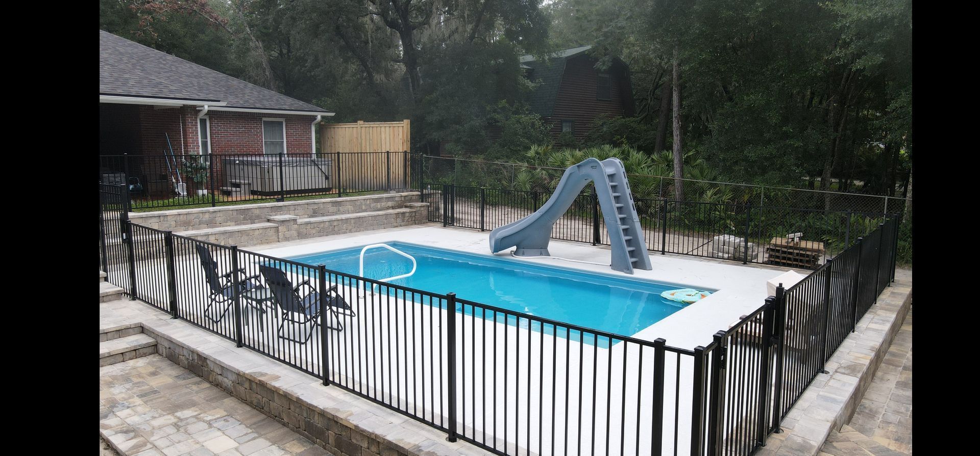 A large swimming pool surrounded by a fence and a slide.