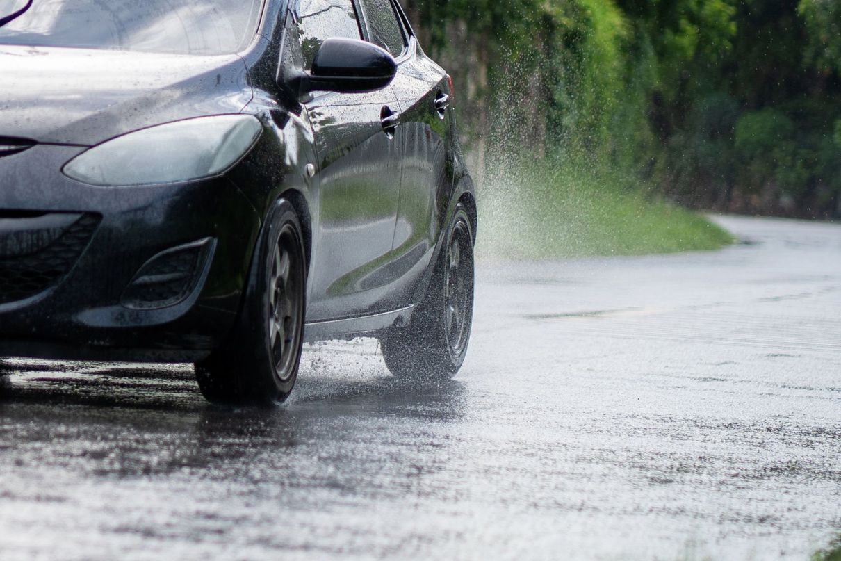 Un'auto nera che percorre una strada resa scivolosa dalla pioggia, sollevando schizzi d'acqua mentre attraversa una pozzanghera.
