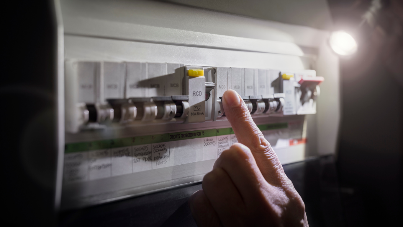 Hand reaching for a circuit breaker switch in a dimly lit electrical panel.