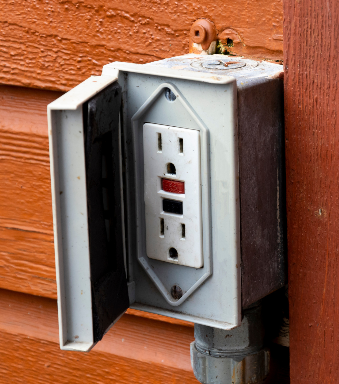 Outdoor electrical outlet with a weather-resistant cover. Red and black buttons on the outlet.