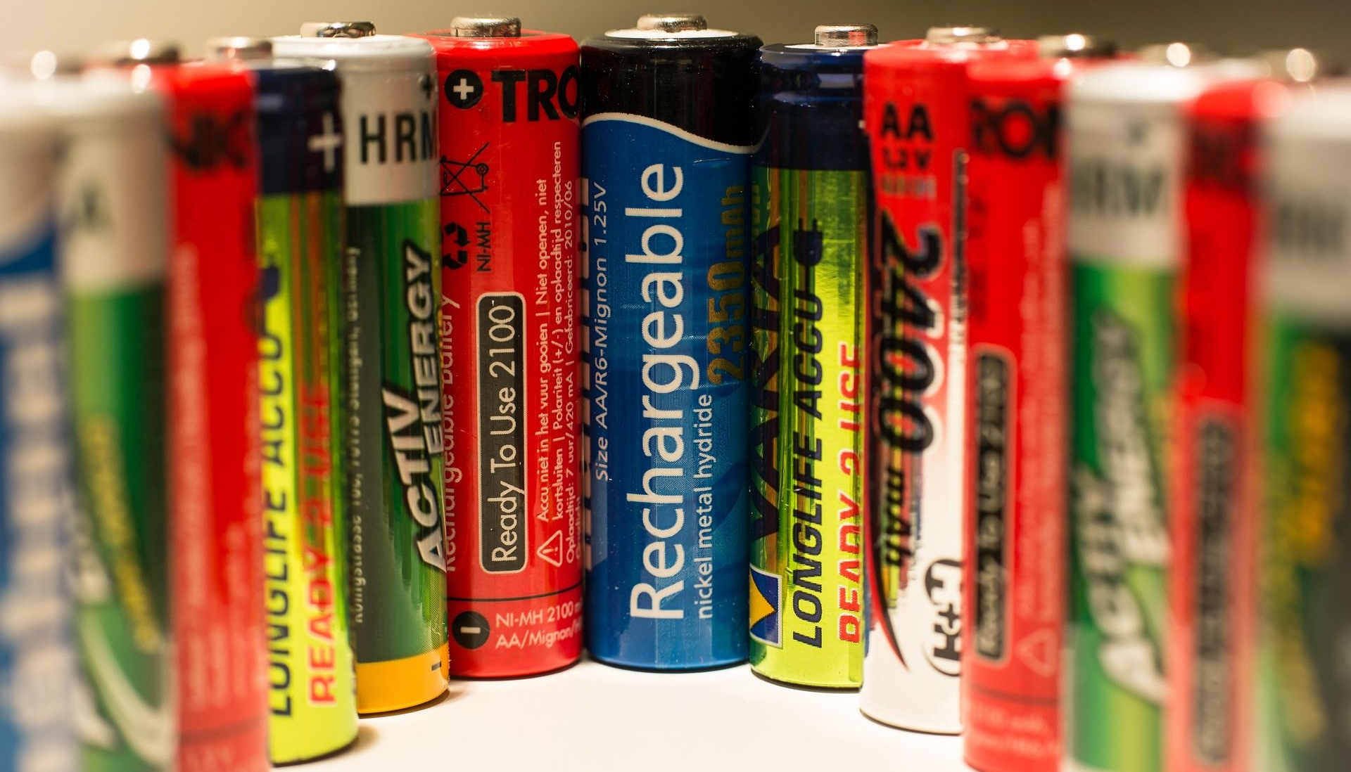A close-up of various colorful AA batteries, including rechargeable ones, arranged upright.