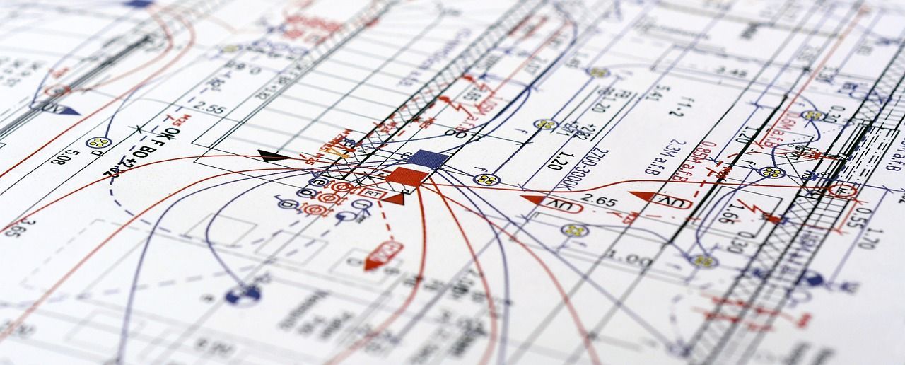 Close-up of a blueprint, featuring lines, symbols, and handwritten text in red and blue on white paper.