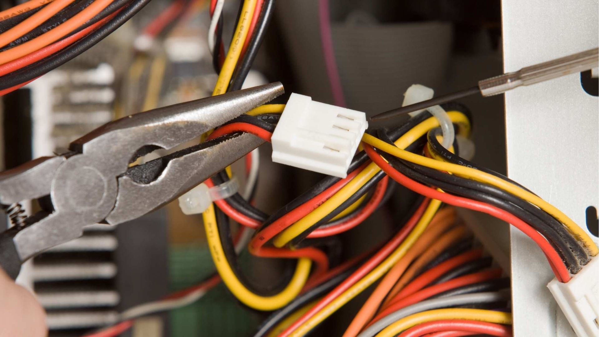 Pliers and screwdriver working on a computer's colorful wires and a white connector inside a computer case.