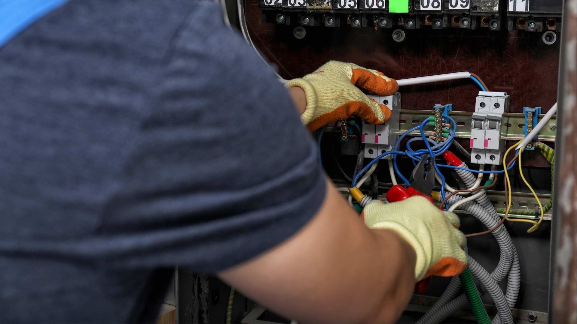 Person wearing gloves working on electrical wiring in a panel.