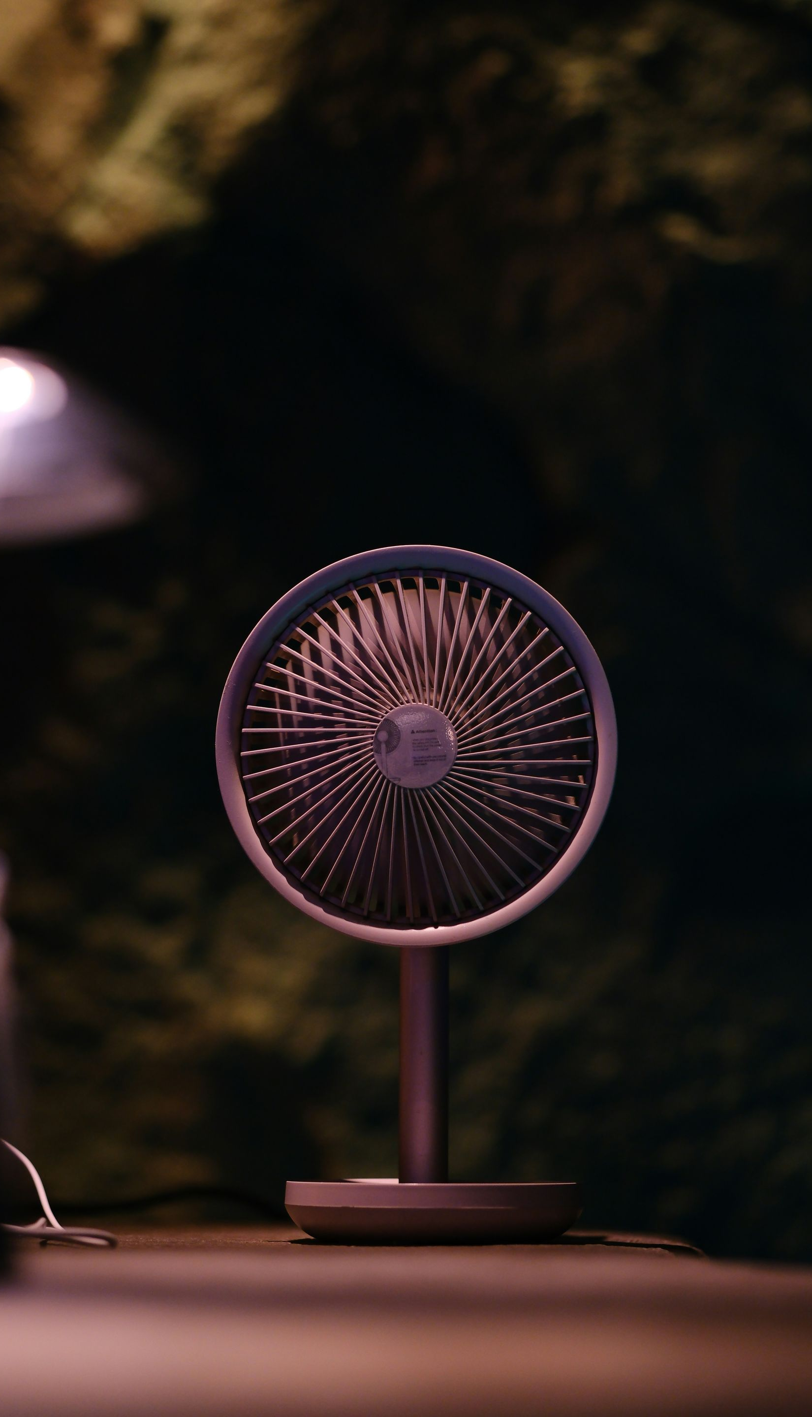 A small, purple desk fan against a blurred, dark green background.