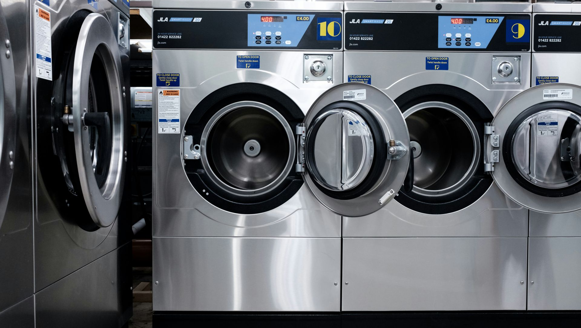Row of open silver washing machines in a laundromat.
