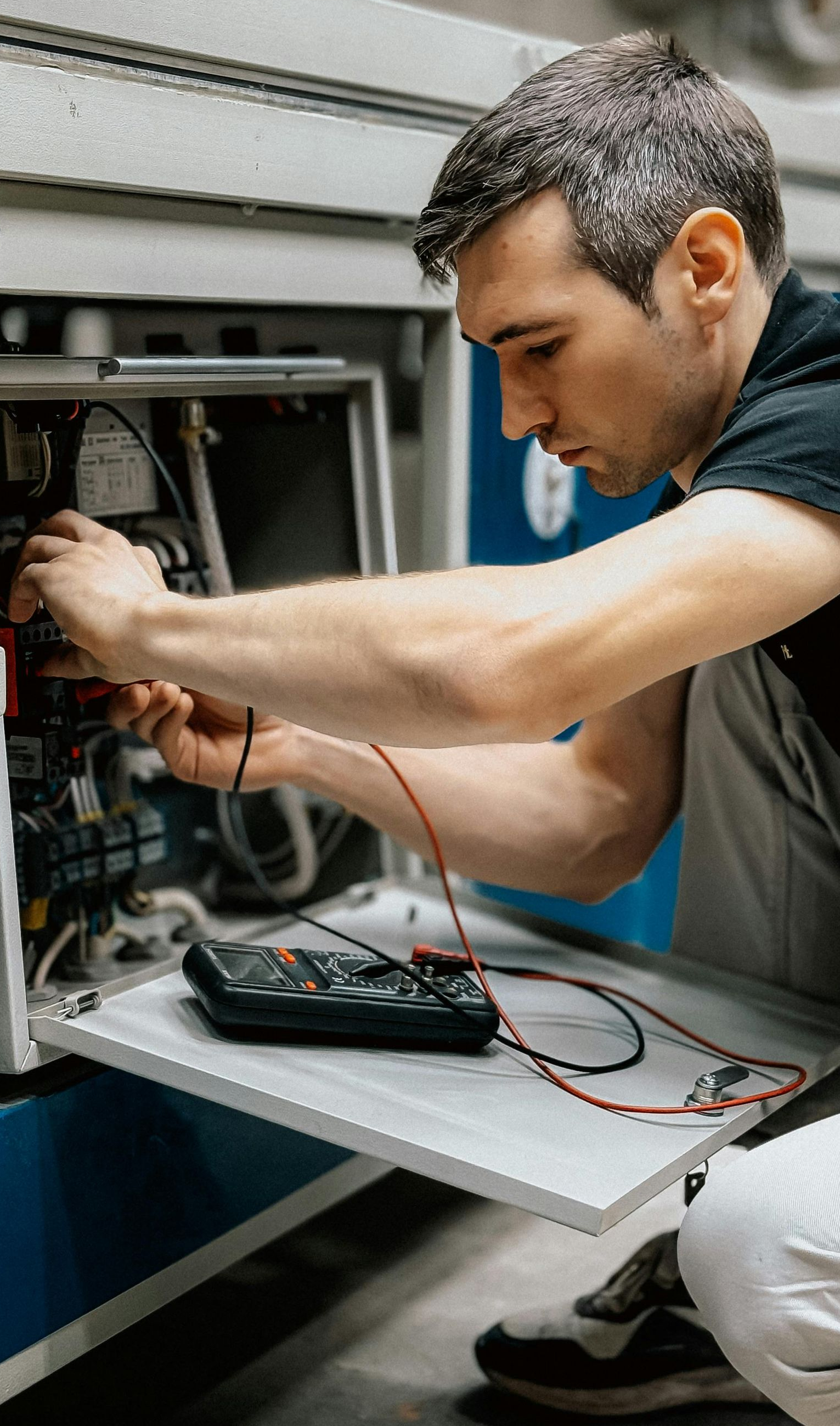 Man working on machinery, using a multimeter; interior setting.