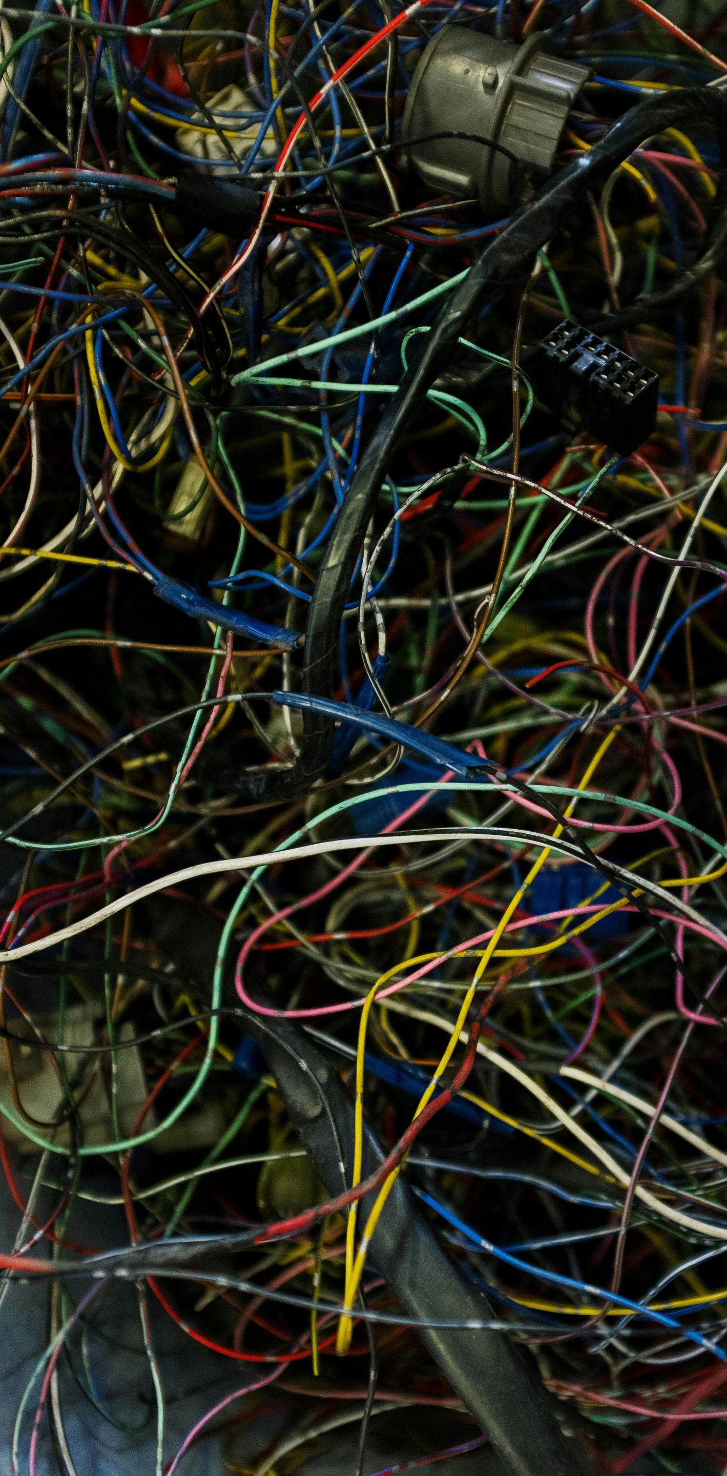 Tangled mess of colorful wires, including red, yellow, blue, green, and white, in a dark setting.