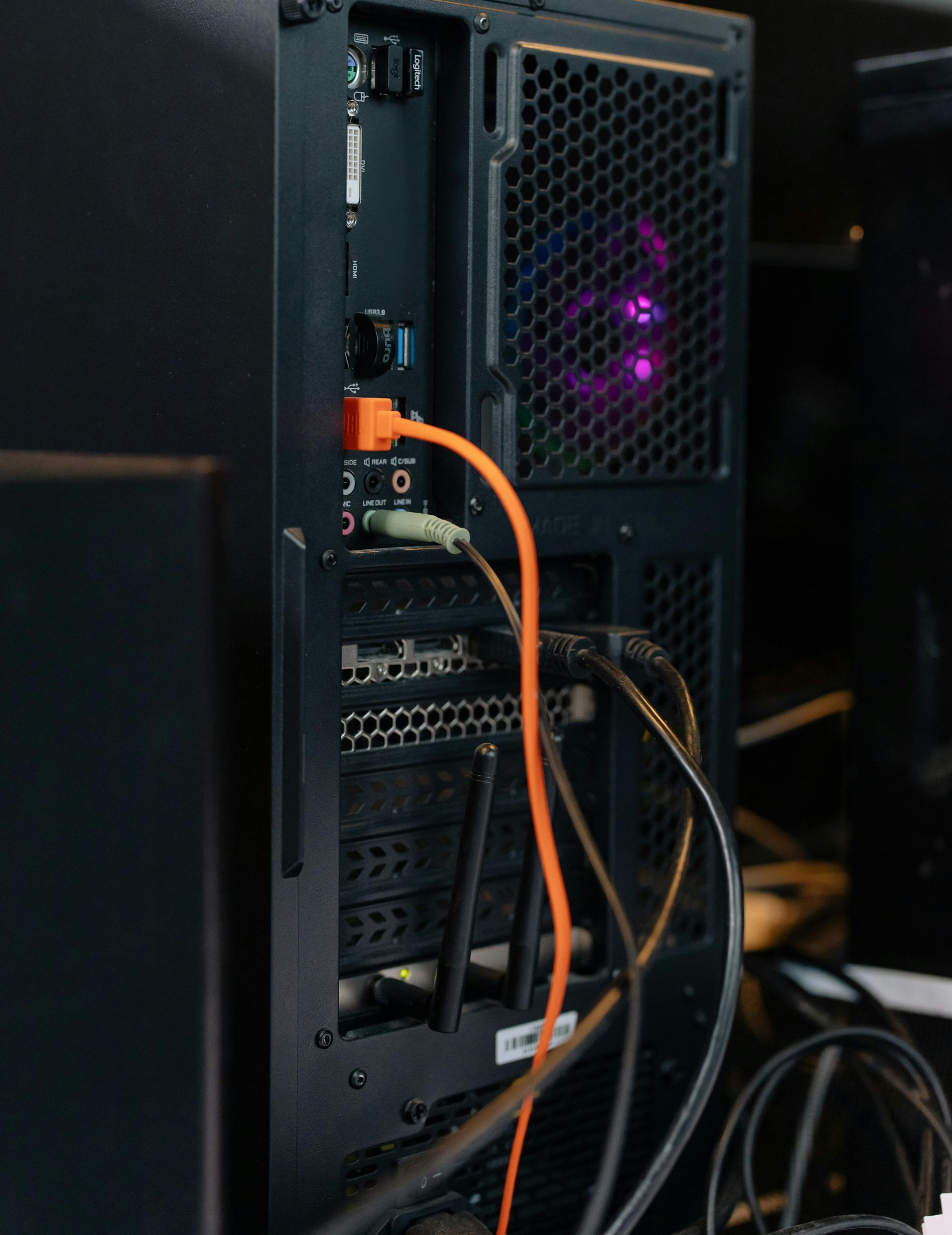 Back of a computer tower with visible ports, cables, and a fan glowing purple. An orange Ethernet cable is plugged in.