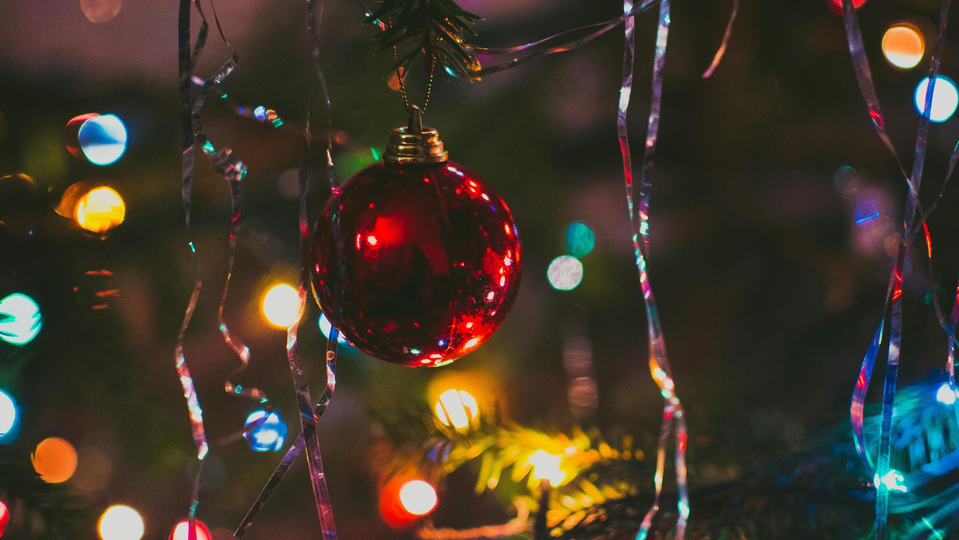 Red Christmas ornament on a tree branch, surrounded by colorful, blurred string lights.