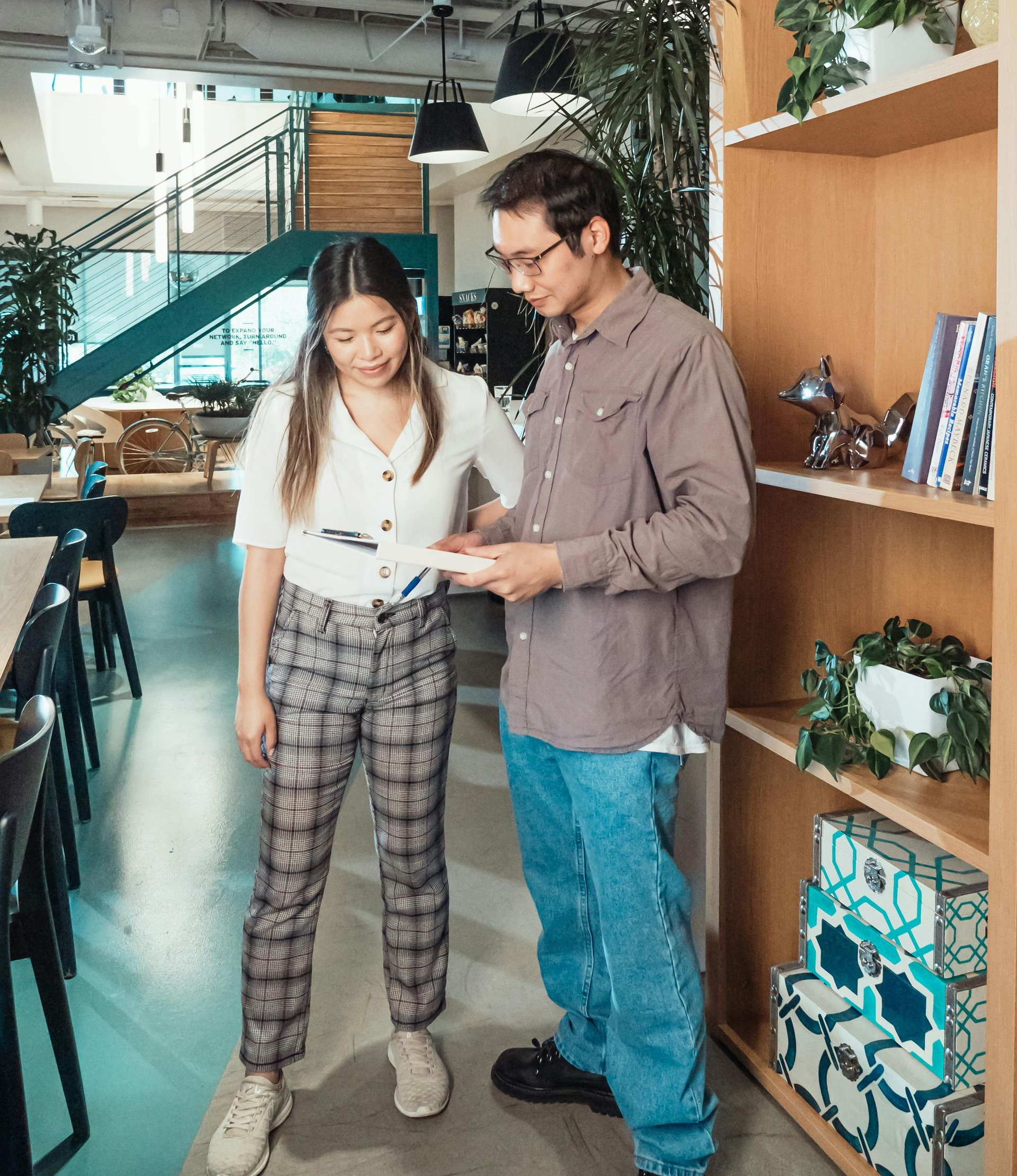 Woman and man looking at papers together in an office setting with shelves and plants.
