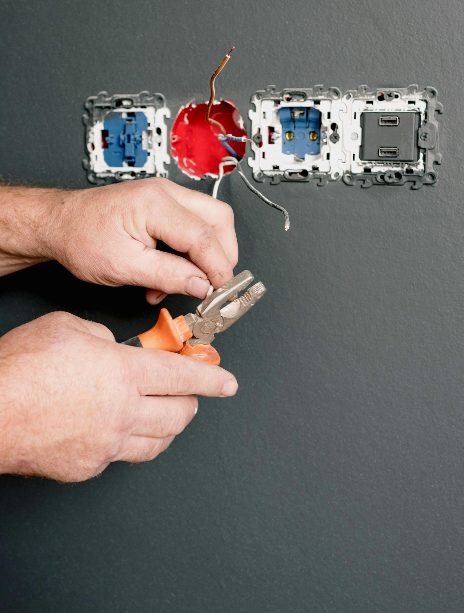 Person using pliers to work on electrical wiring in a wall.