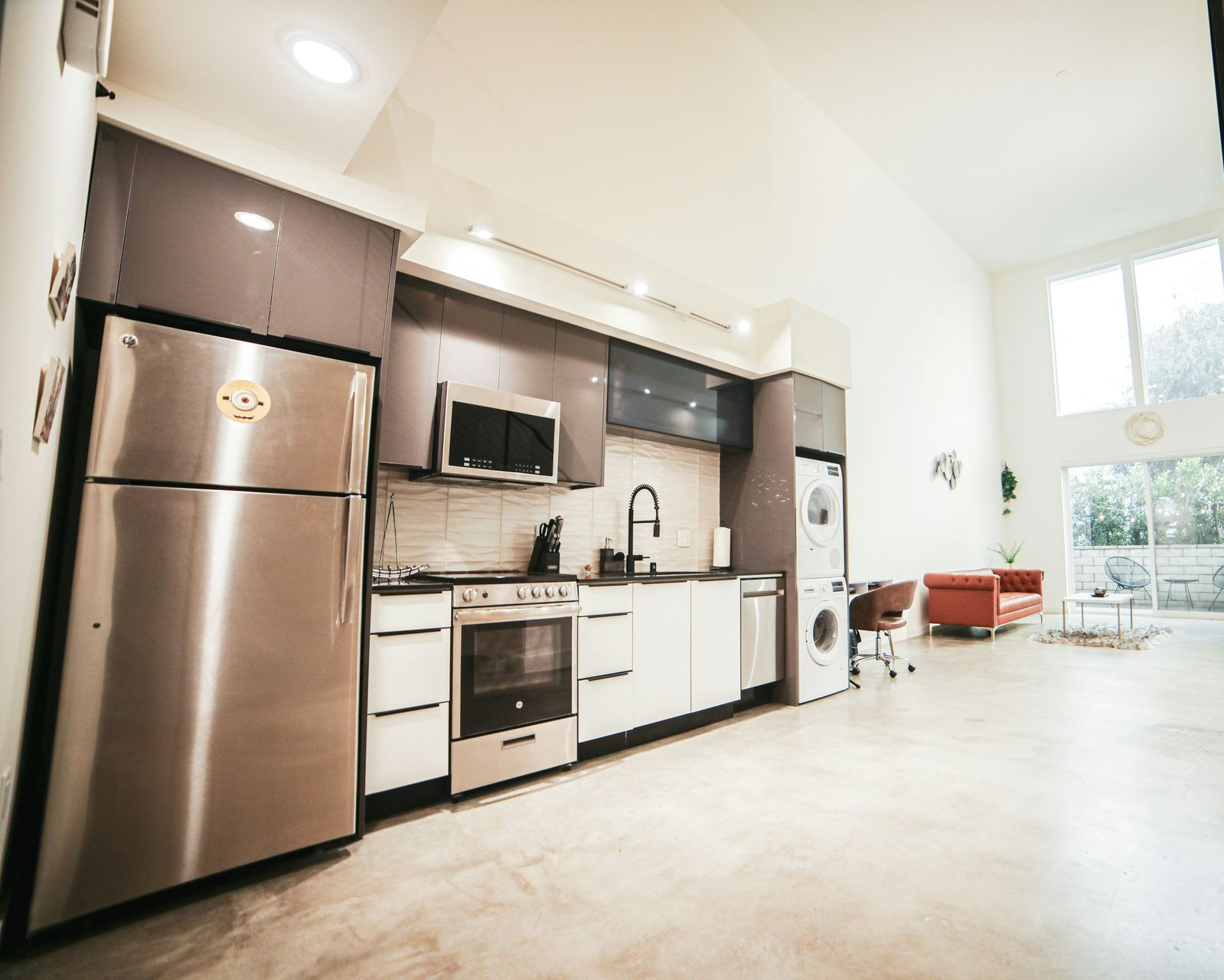 Modern kitchen with stainless steel appliances, white cabinets, and a high ceiling.
