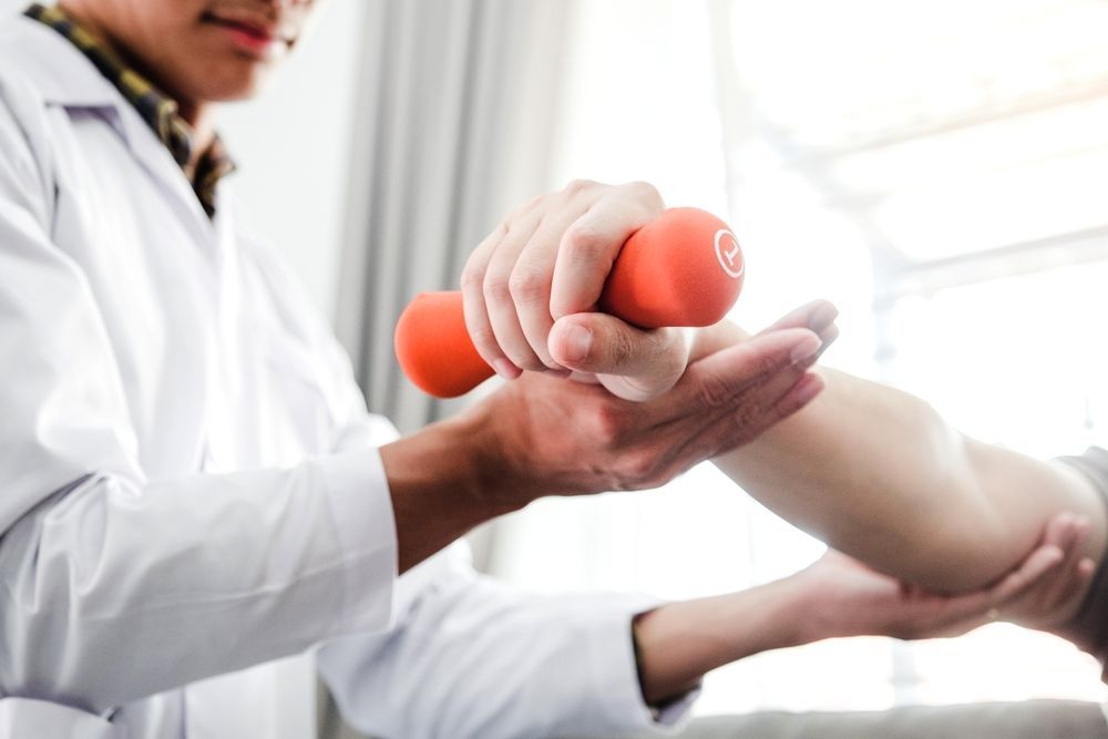 A Doctor is Helping a Patient With a Dumbbell — PhysioCare Townsville In  Townsville, QLD