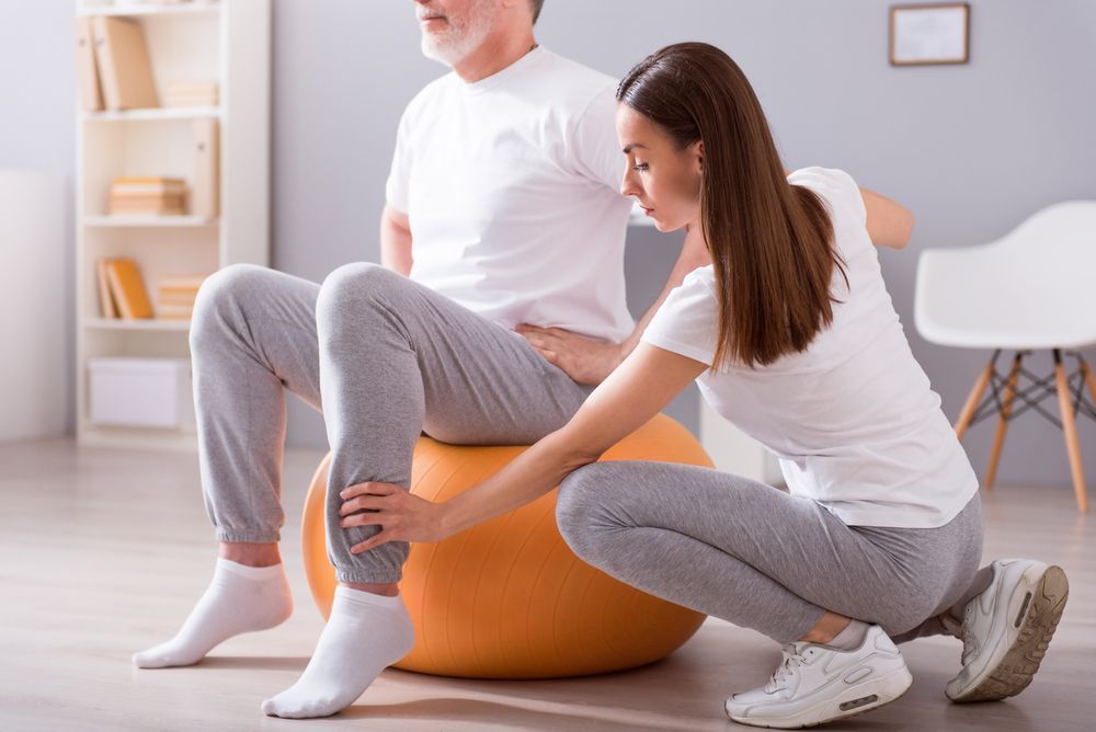 A Woman is Helping a Man Sit on a Exercise Ball — PhysioCare Townsville In Thuringowa Central, QLD