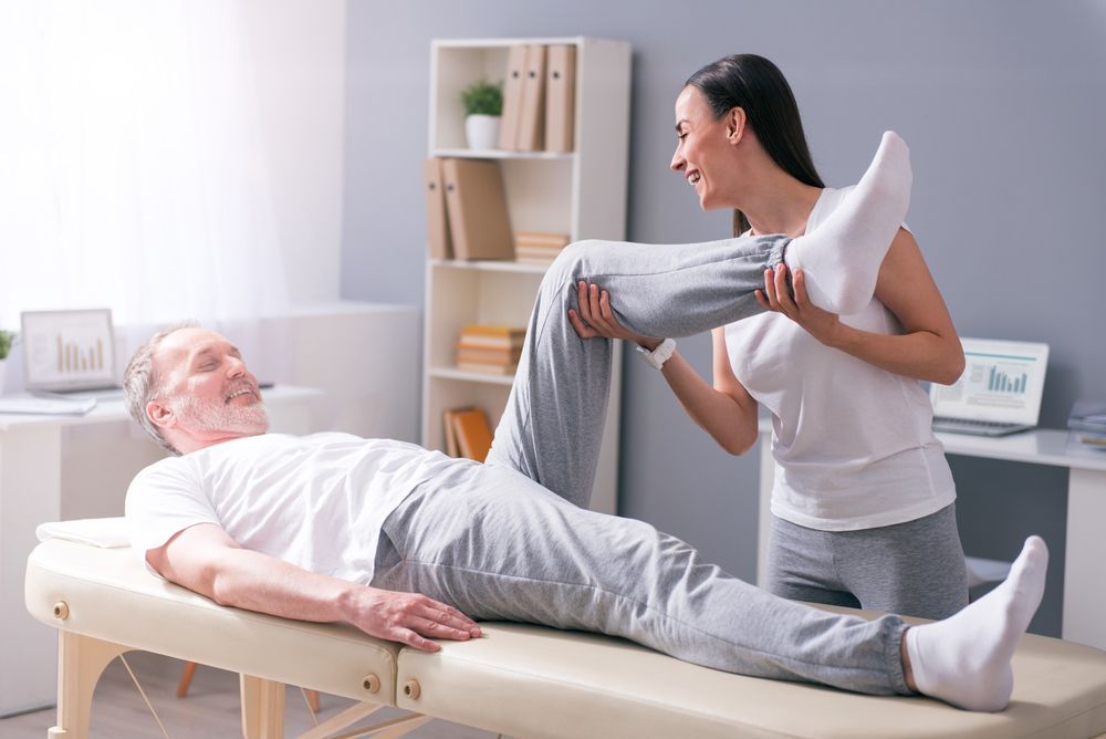 A Woman is Stretching a Man 's Leg on a Table — PhysioCare Townsville In Thuringowa Central, QLD