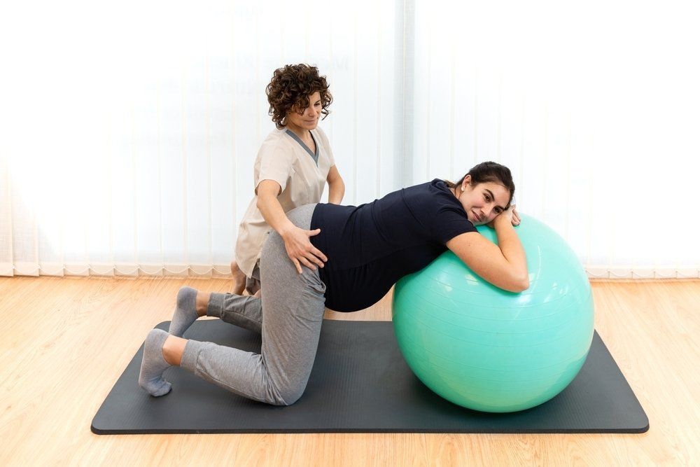 A Pregnant Woman Doing Pilates Exercises With a Ball With the Help of Her Physiotherapist — PhysioCare Townsville In Thuringowa Central, QLD