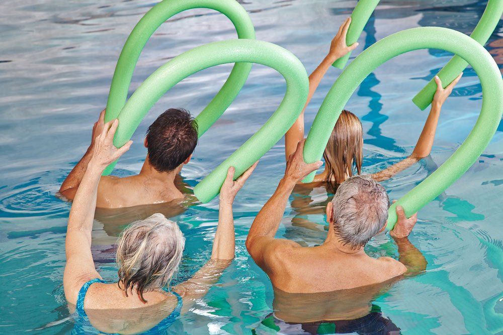 Group of Senior People Doing Aqua Fitness From Behind With Swim Noodles — PhysioCare Townsville In Thuringowa Central, QLD