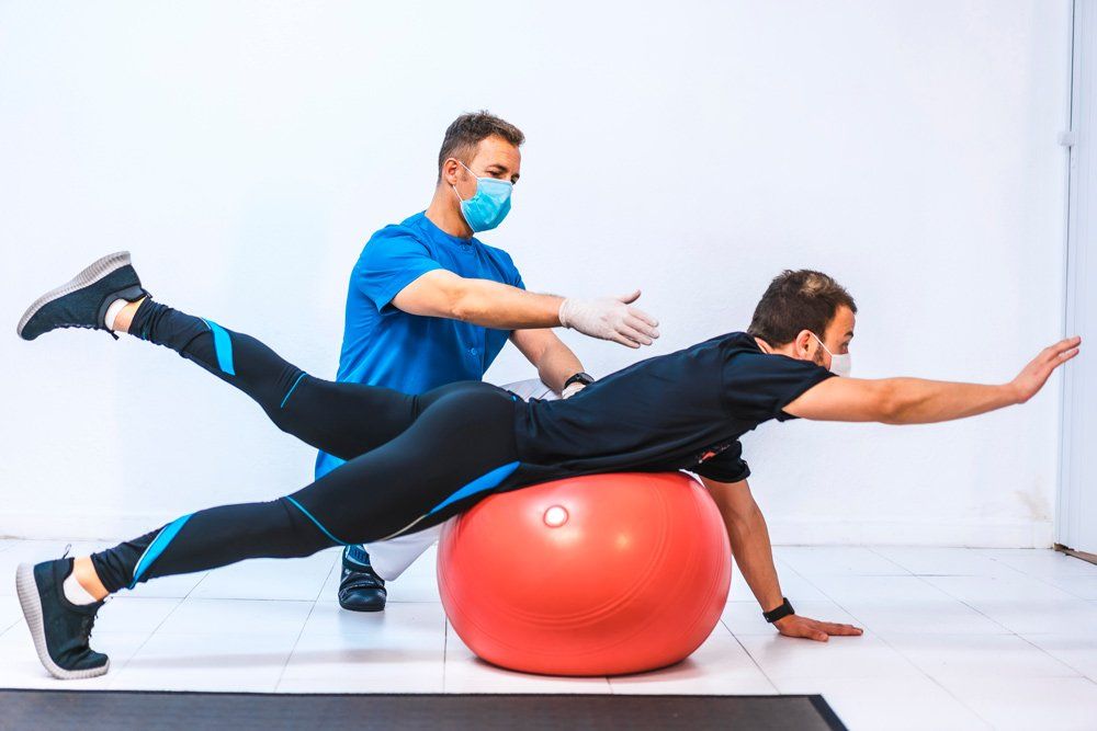 Physiotherapist With Mask and a Patient Stretching on a Ball — PhysioCare Townsville In Thuringowa Central, QLD