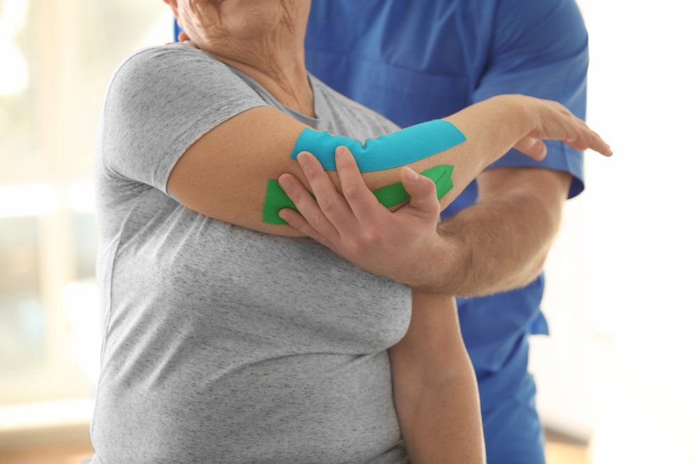 Physiotherapist Working With Elderly Patient Shoulder With Kinesiotaping — PhysioCare Townsville In Thuringowa Central, QLD