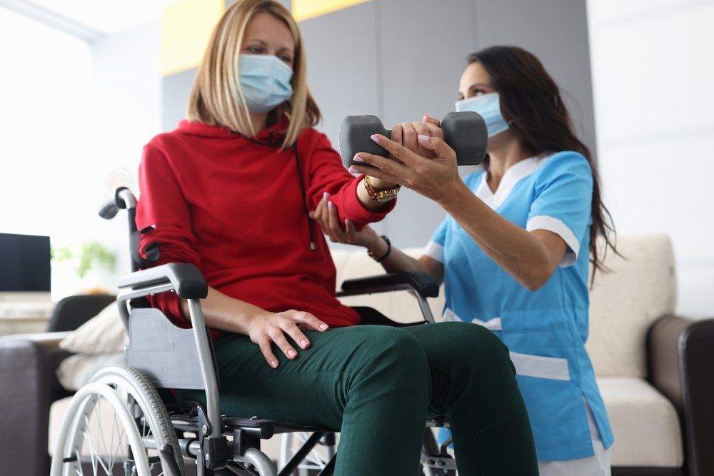 Physiotherapist Doctor in Medical Mask Helps to Raise Dumbbell — PhysioCare Townsville In Thuringowa Central, QLD