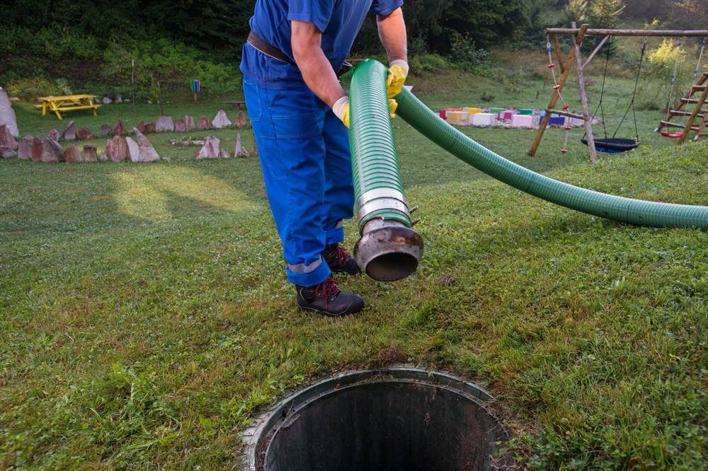 A Man is Pumping Sewage Into a Manhole With a Green Hose — Glenview Septic & Liquid Waste Removal In Caboolture, QLD