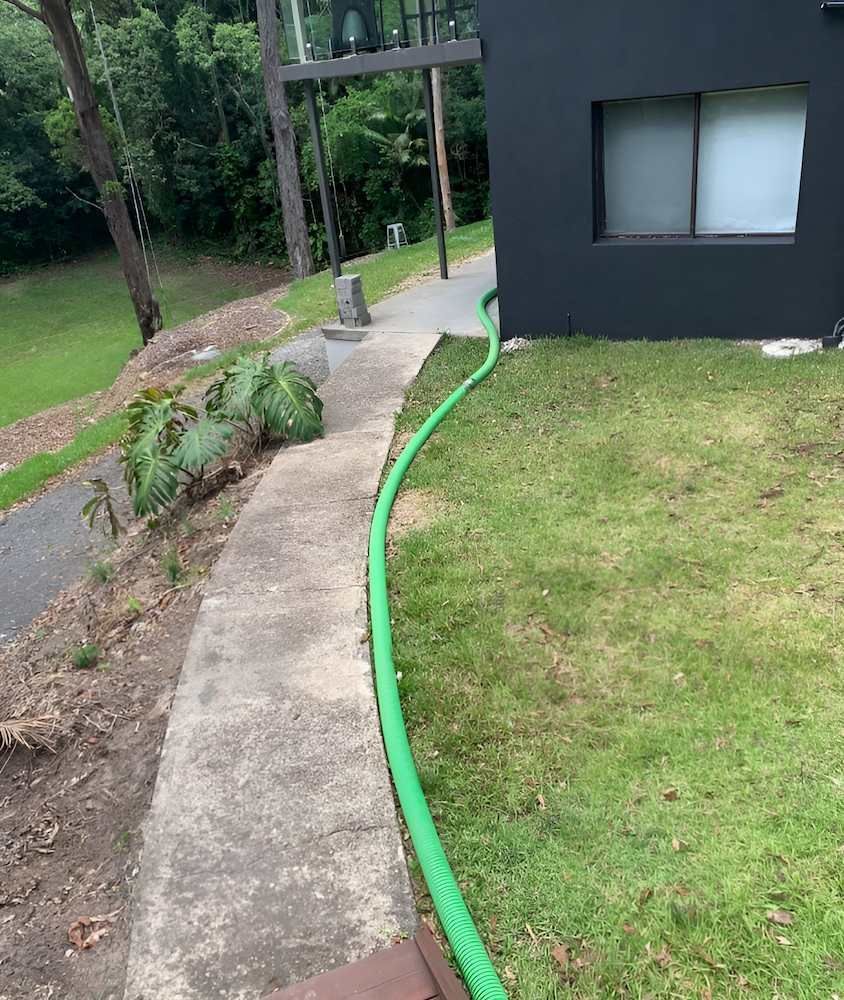 A Green Hose is Connected to a Sidewalk Next to a House — Glenview Septic & Liquid Waste Removal In Beerwah, QLD