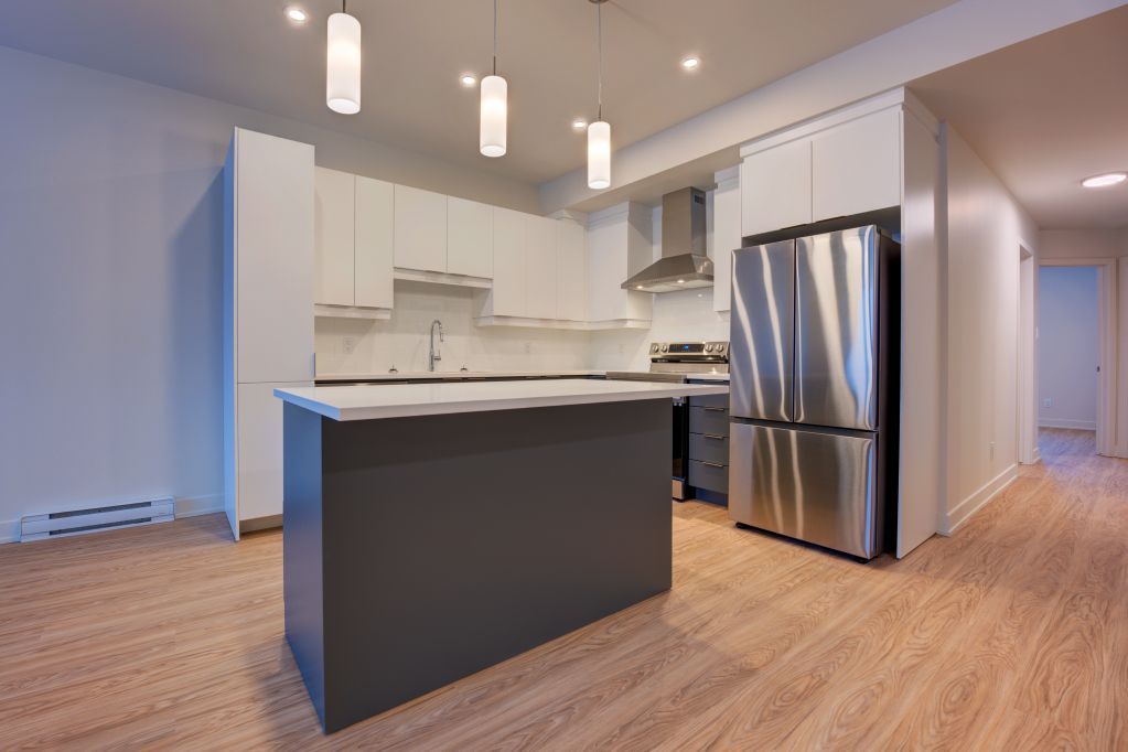 Cuisine moderne avec réfrigérateur en acier inoxydable, armoires blanches, îlot et parquet.