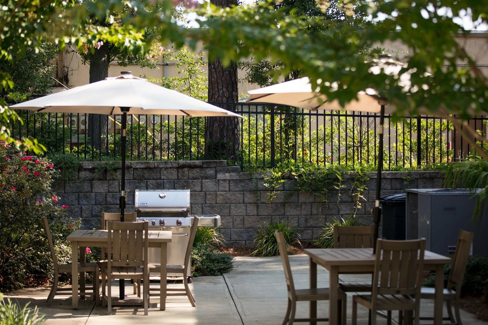 Outdoor patio with wooden tables, beige umbrellas, and a stone wall in the background  at Arcadia's Edge Apartments in Columbia, SC