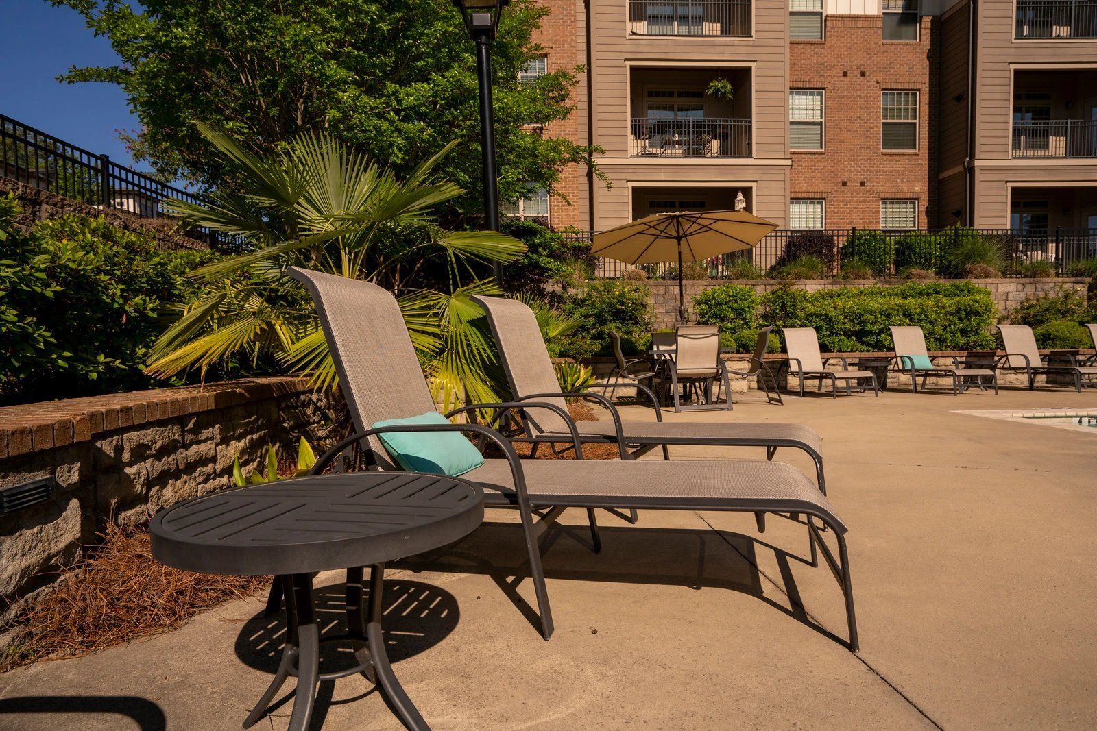 Poolside lounge chairs and a round table in a sunny courtyard with a brick apartment building backdrop  at Arcadia's Edge Apartments in Columbia, SC
