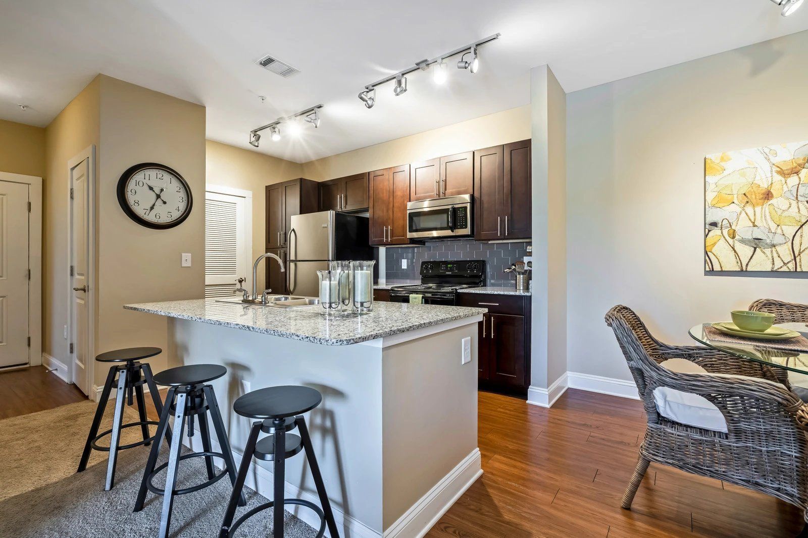 Open-plan kitchen and dining area with granite island, bar stools, stainless appliances, and hardwood floors  at Arcadia's Edge Apartments in Columbia, SC