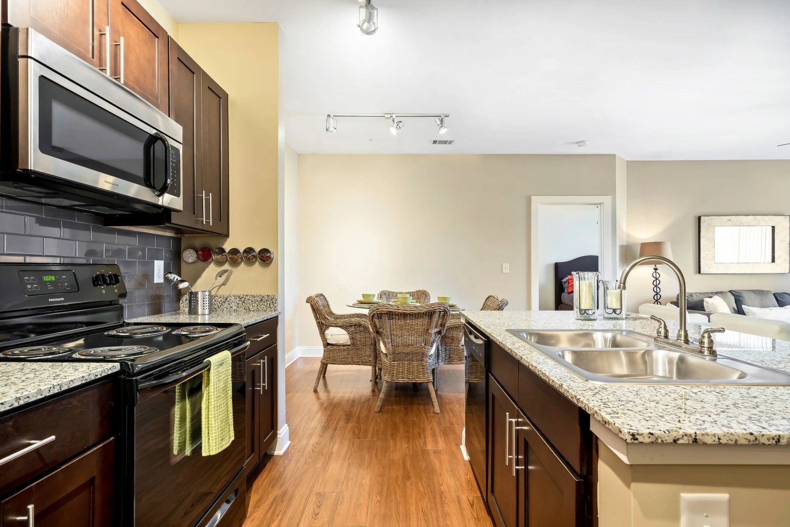 Modern kitchen with granite island, dark wood cabinets, and dining area in the background at Arcadia's Edge Apartments in Columbia, SC