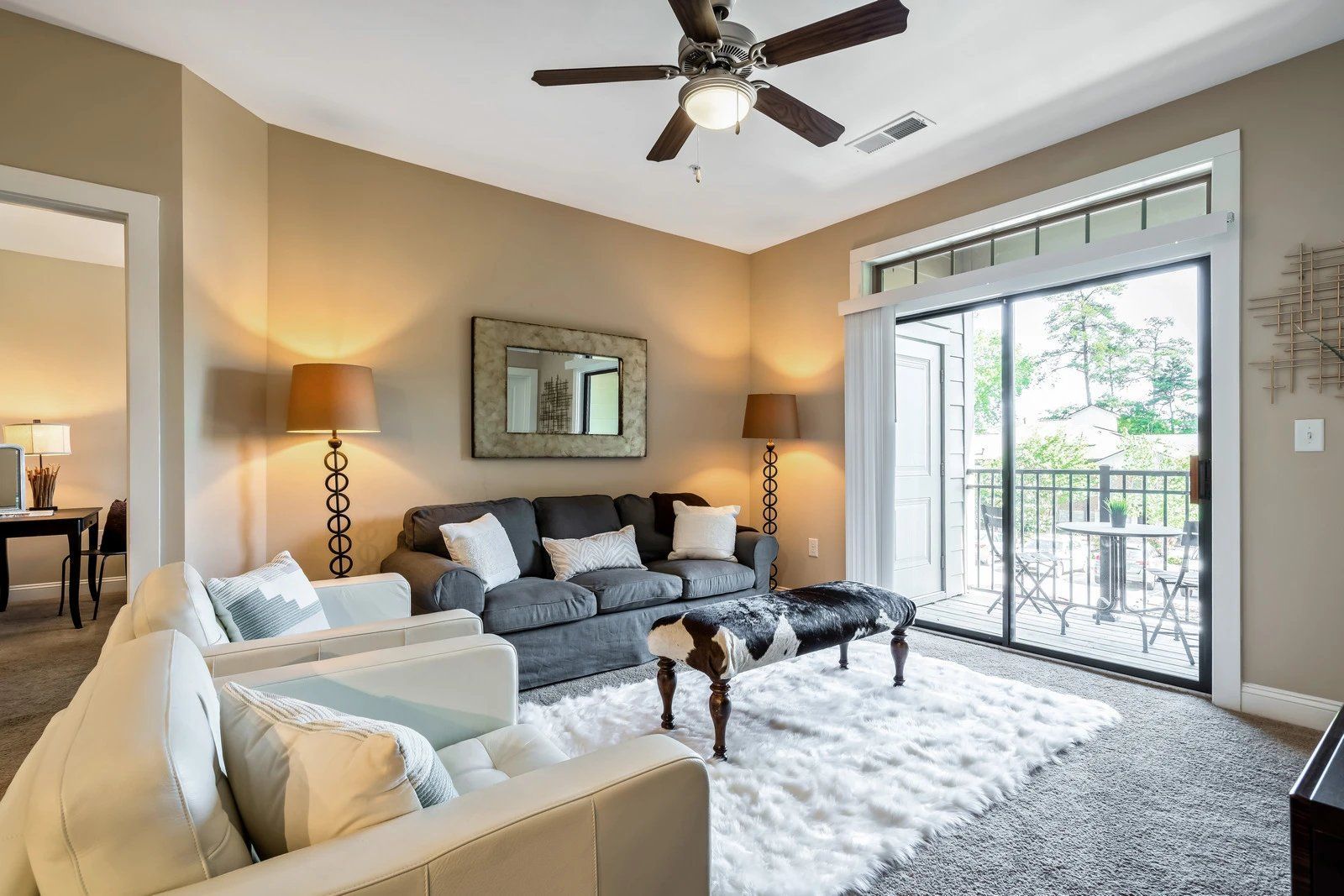 Bright living room with gray sofa, beige chairs, fireplace, ceiling fan, and balcony doors open to greenery  at Arcadia's Edge Apartments in Columbia, SC