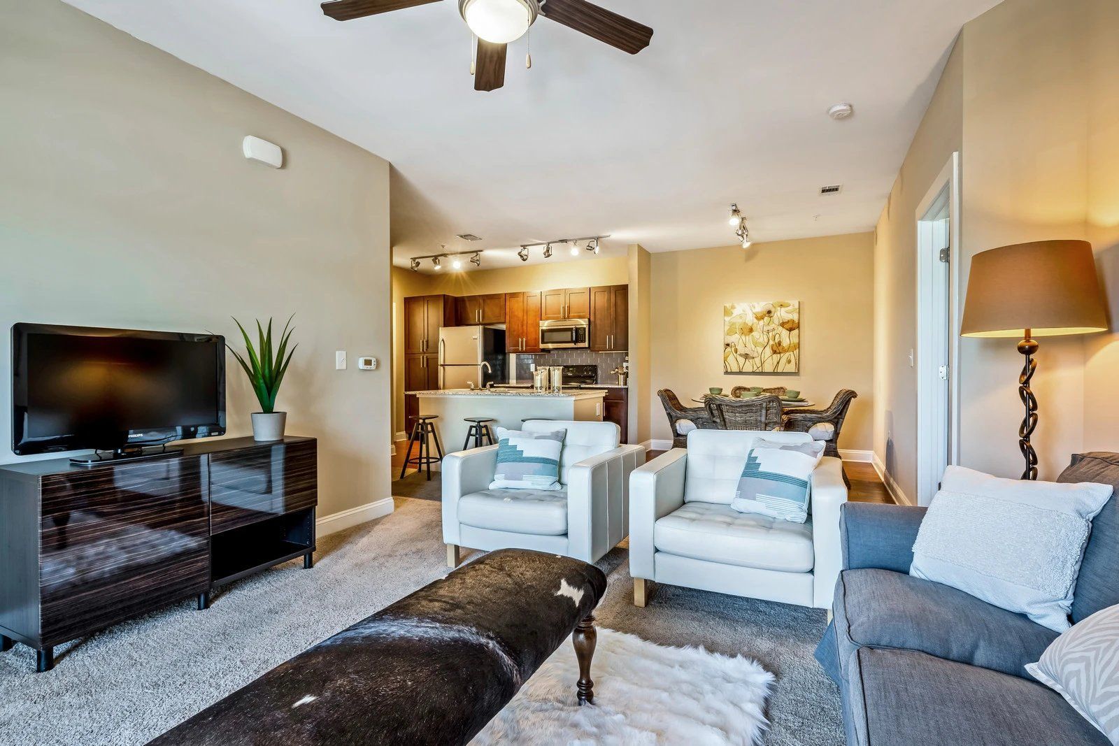 Bright living room with sofa, armchairs, TV, and open kitchen in the background  at Arcadia's Edge Apartments in Columbia, SC