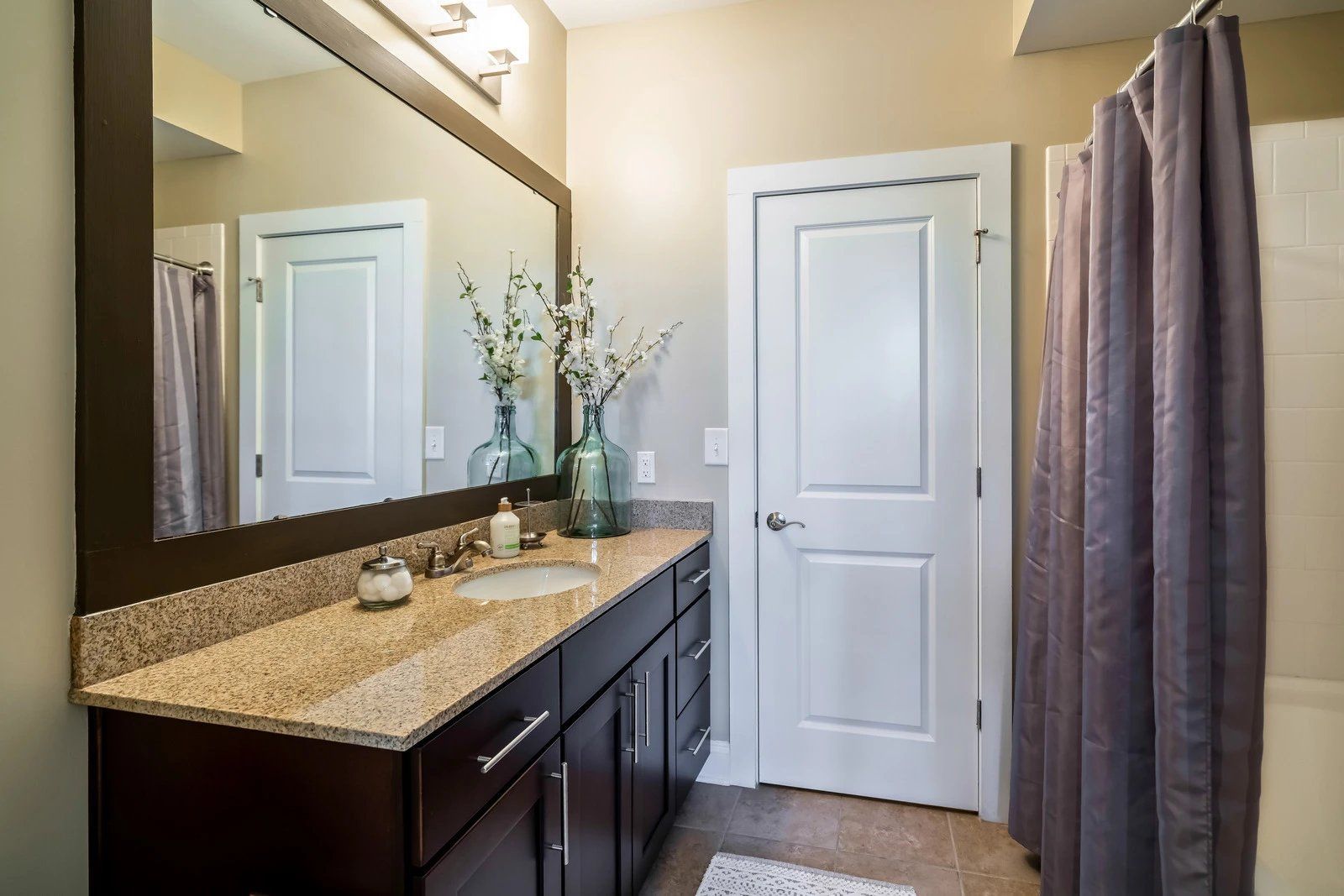 Bathroom vanity with granite countertop, large mirror, white door, and a shower curtain  at Arcadia's Edge Apartments in Columbia, SC