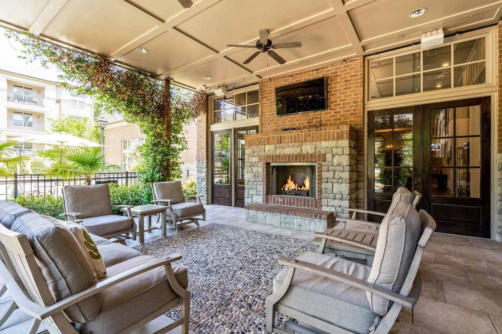 Covered patio with cushioned chairs and a brick fireplace, overlooking a bright outdoor space  at Arcadia's Edge Apartments in Columbia, SC