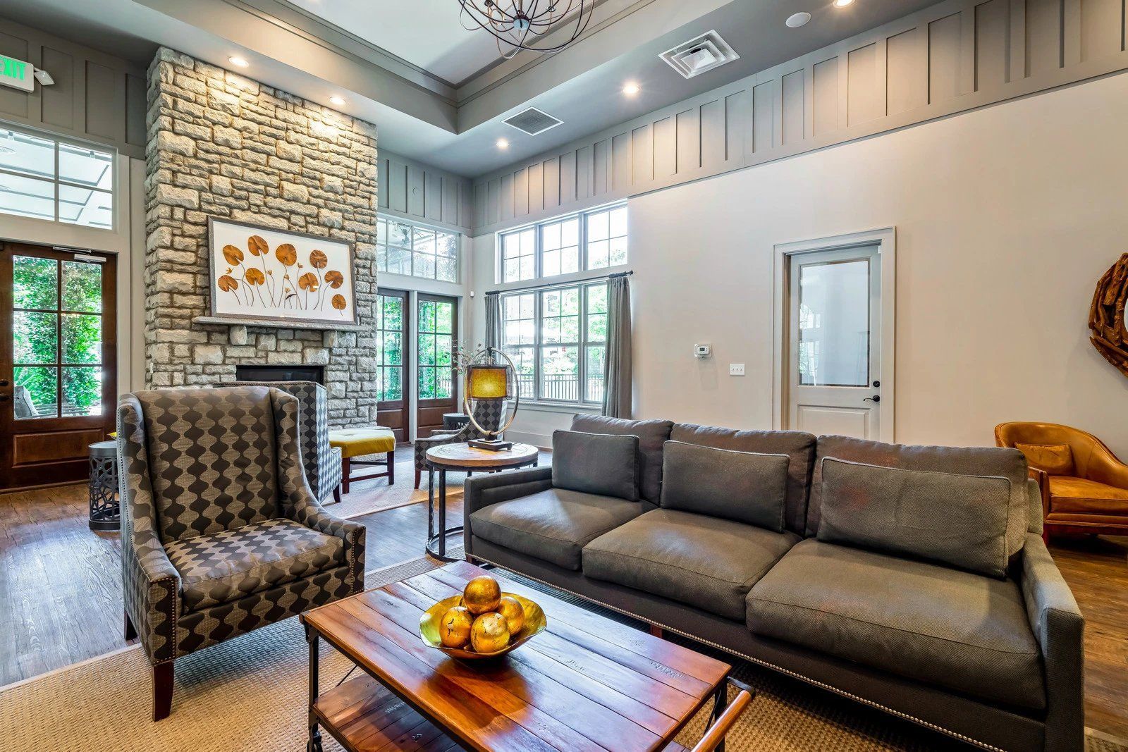 Modern living room with gray sofa, patterned chair, wood coffee table, and stone fireplace near large windows  at Arcadia's Edge Apartments in Columbia, SC