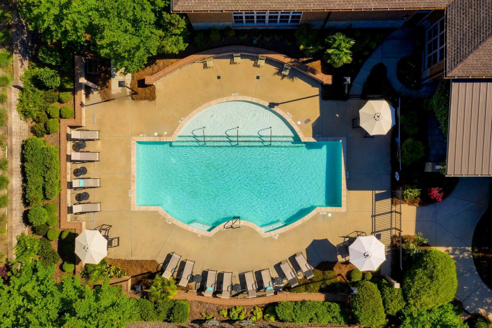 Overhead view of a resort pool with lounge chairs, umbrellas, and surrounding greenery  at Arcadia's Edge Apartments in Columbia, SC