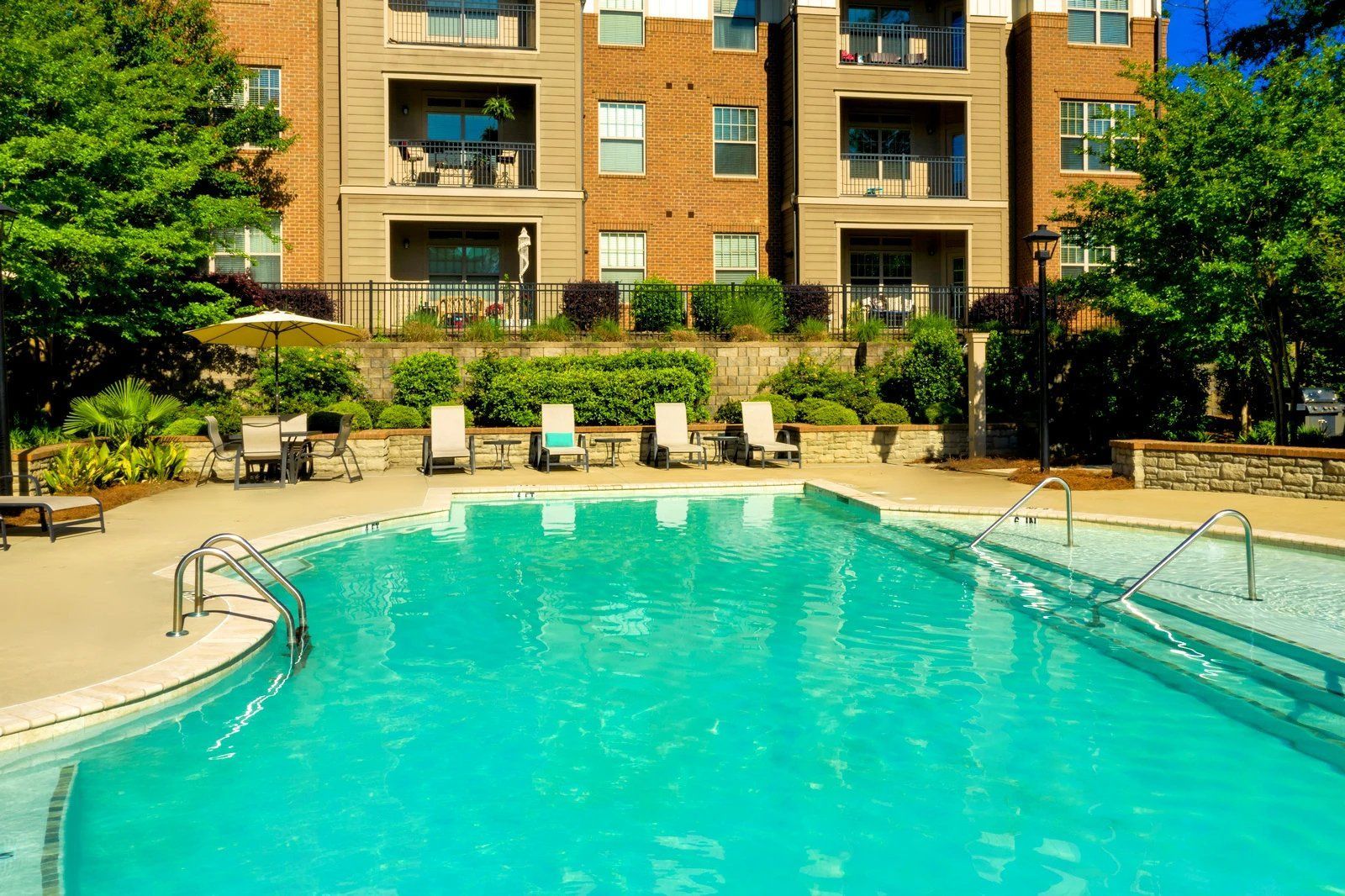 Outdoor apartment pool with turquoise water, lounge chairs, and a brick residential building behind it  at Arcadia's Edge Apartments in Columbia, SC