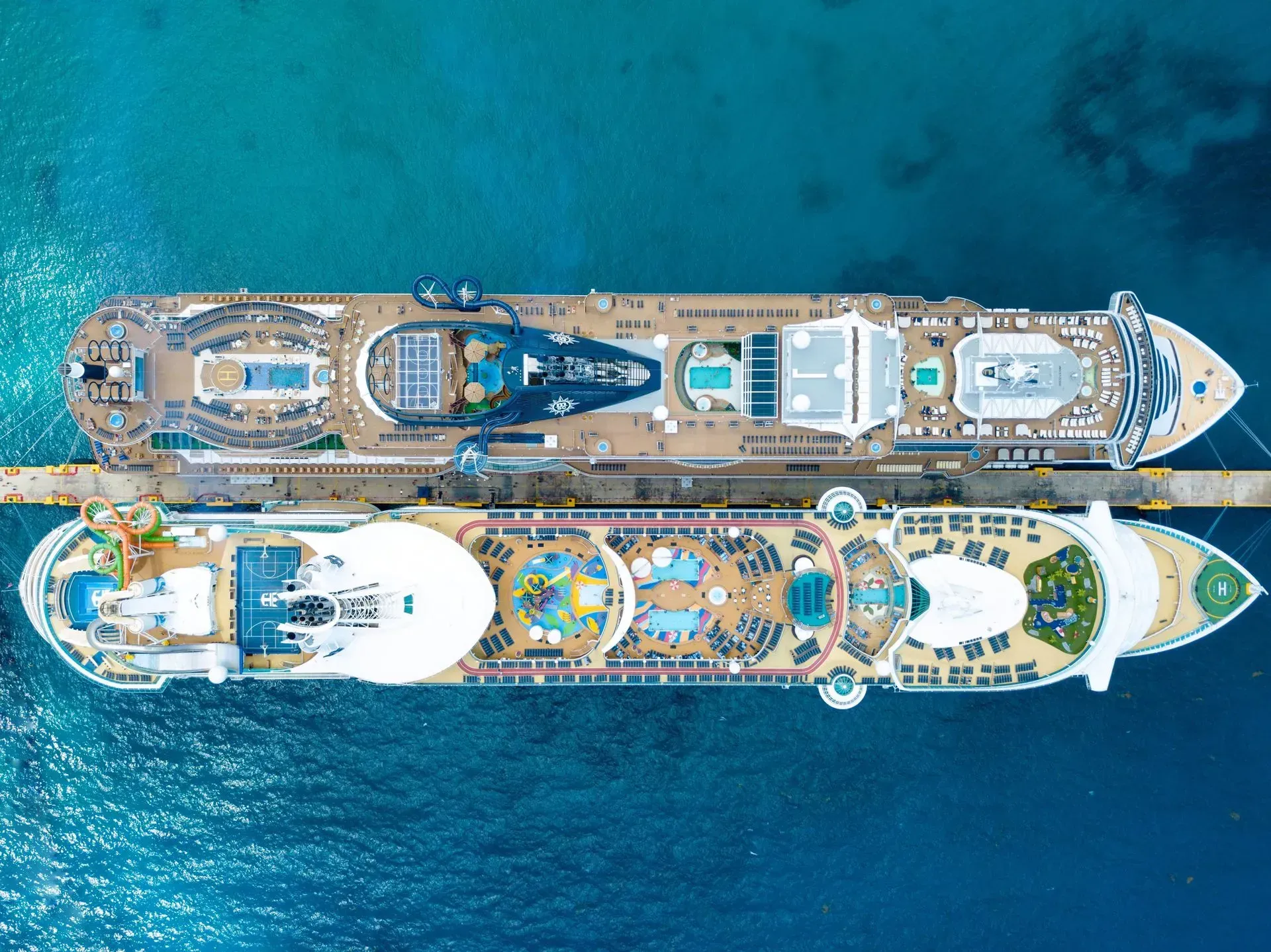 Two cruise ships docked side-by-side in blue water, viewed from above, showcasing decks and amenities.