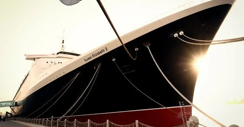 Queen Elizabeth 2 cruise ship docked, black and white hull, red waterline, ropes tied to the pier.