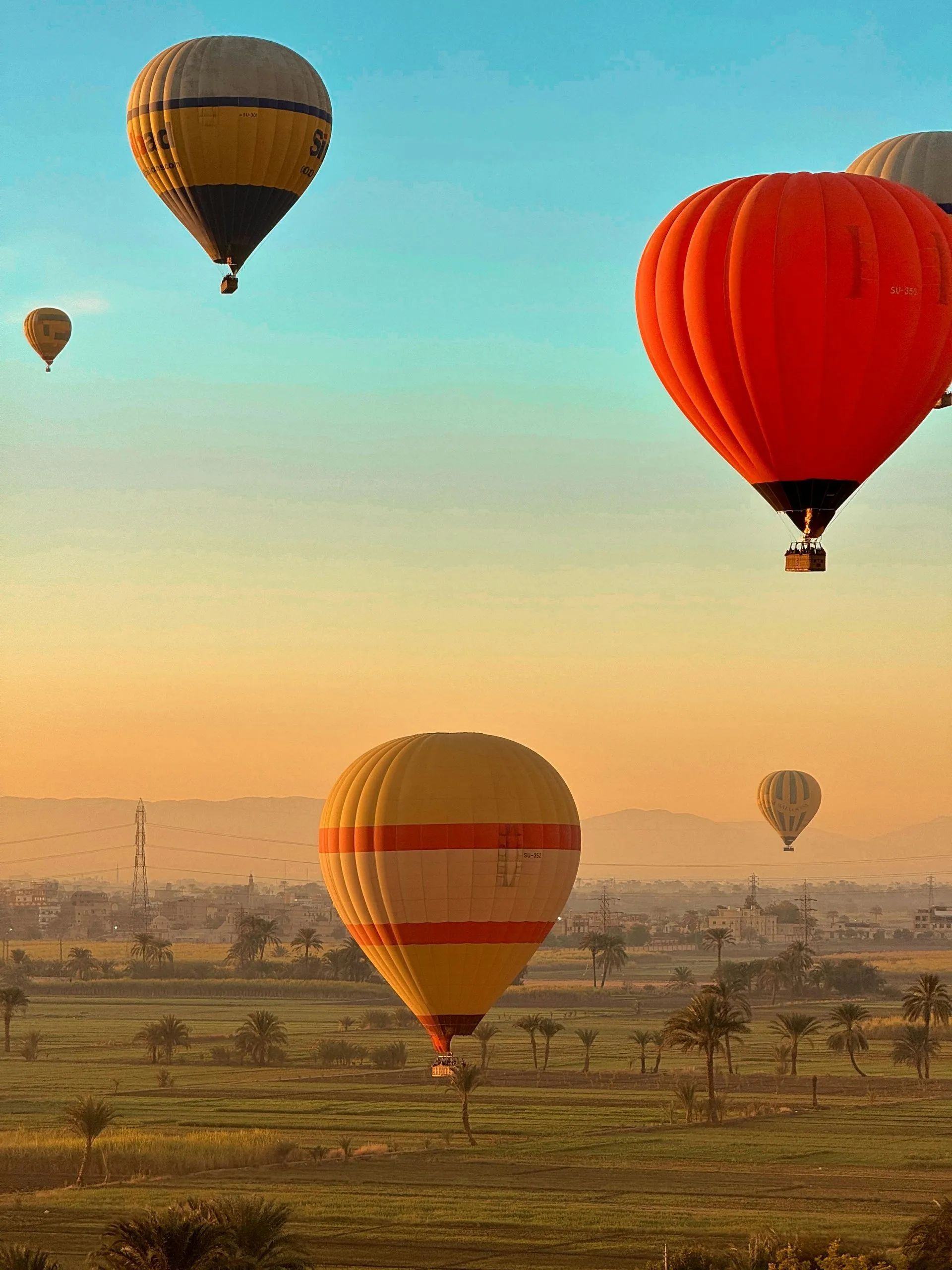 Hot air balloons float over a vast green landscape under a colorful sky at dawn.