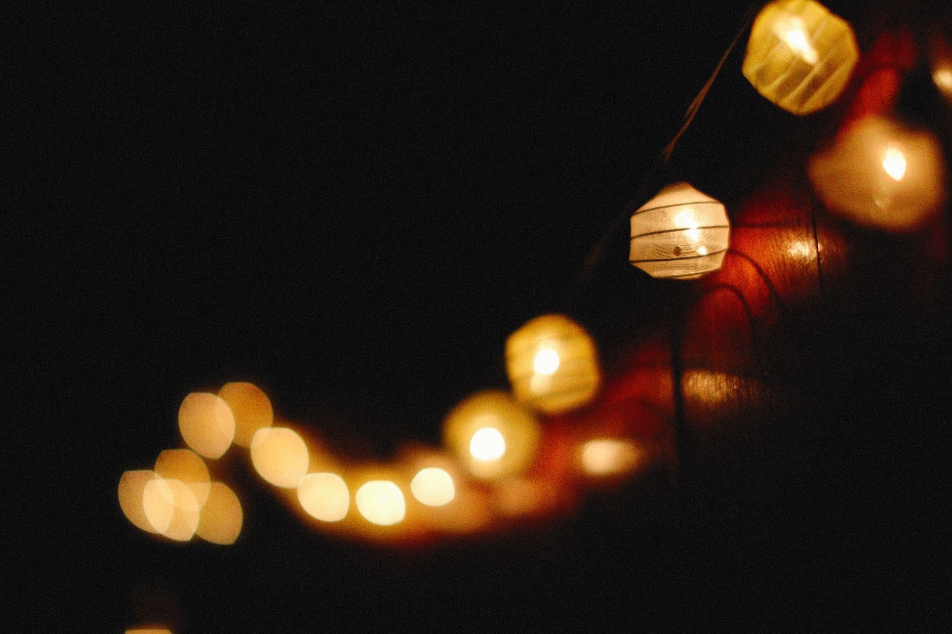 A string of round paper lanterns glows softly with warm golden light against a dark, shadowy night background.