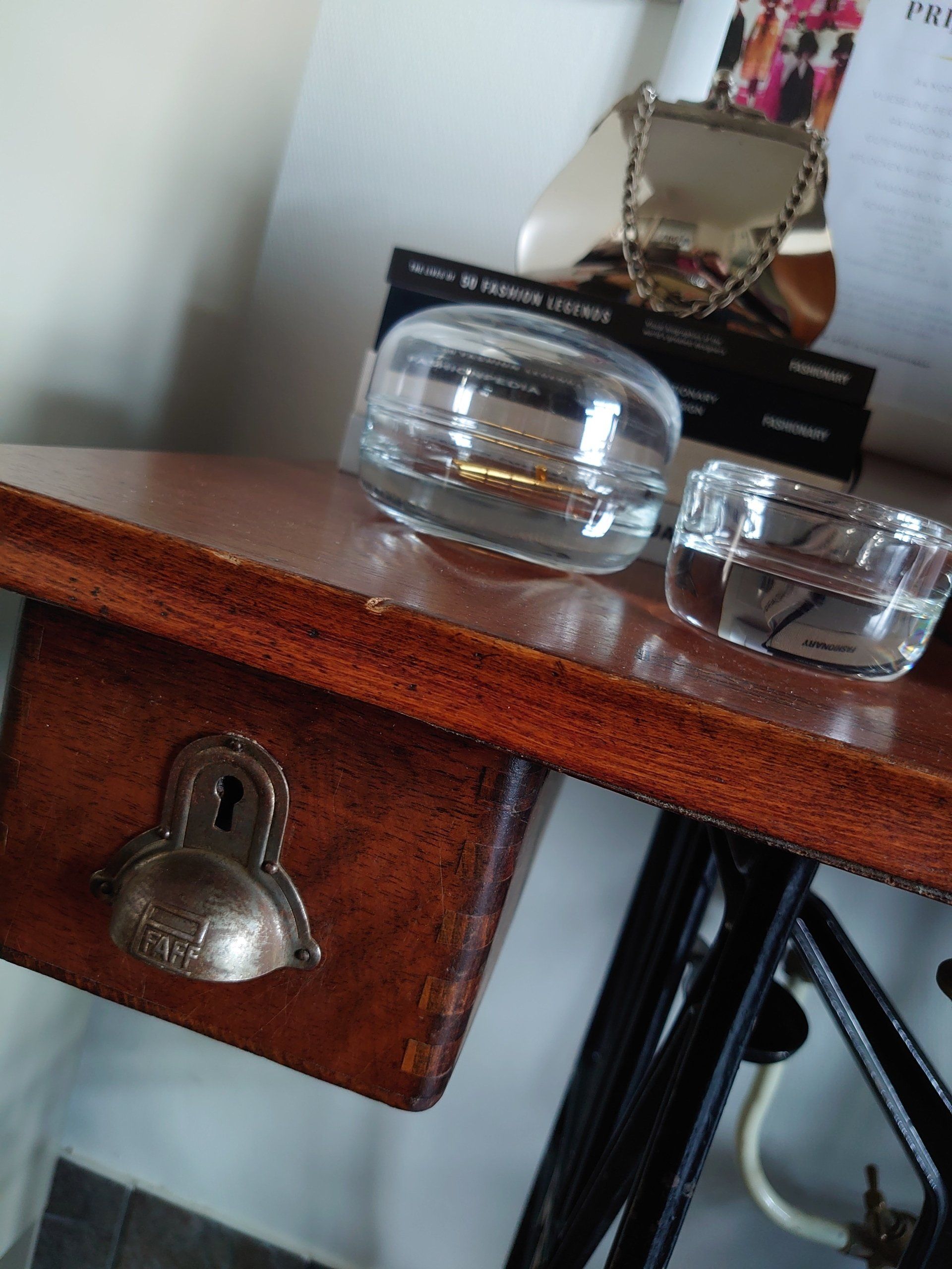Doorzichtige glazen schalen op een houten lade met een metalen knop en een make-upspiegel op de achtergrond.