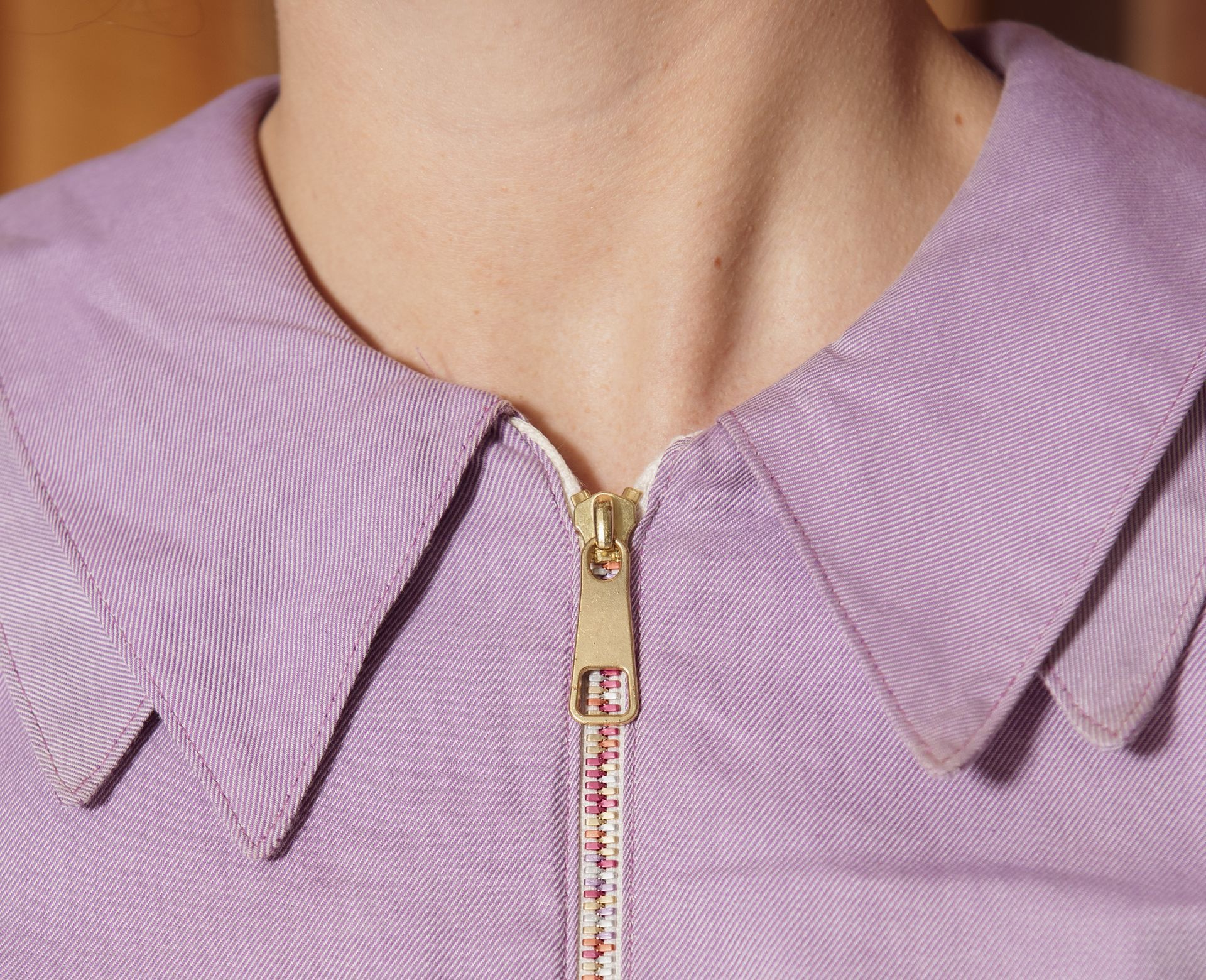 Detailopname van een lavendelkleurige top met kraag en gouden ritssluiting.