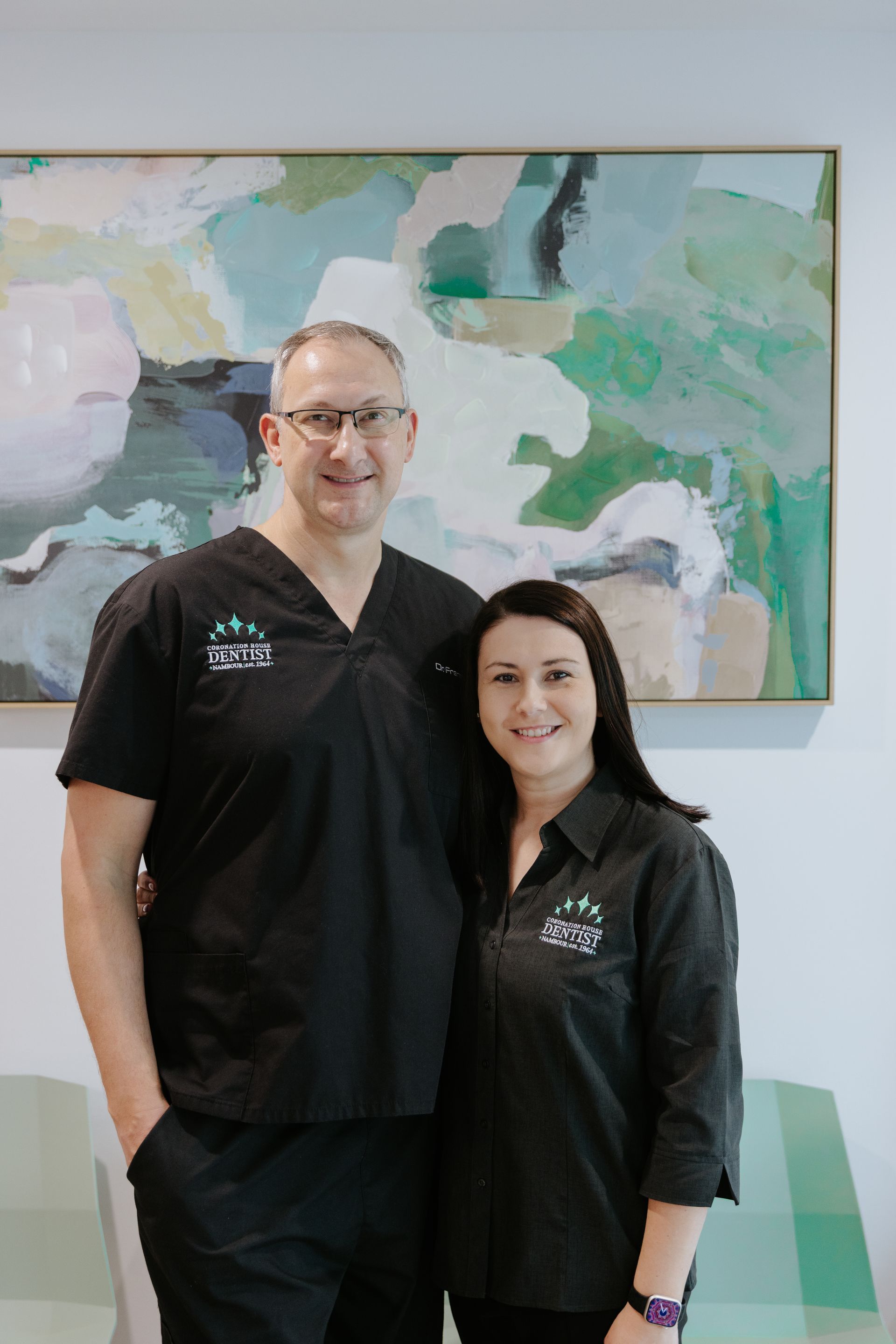 Two staff members in black scrubs stand smiling in front of abstract wall art.