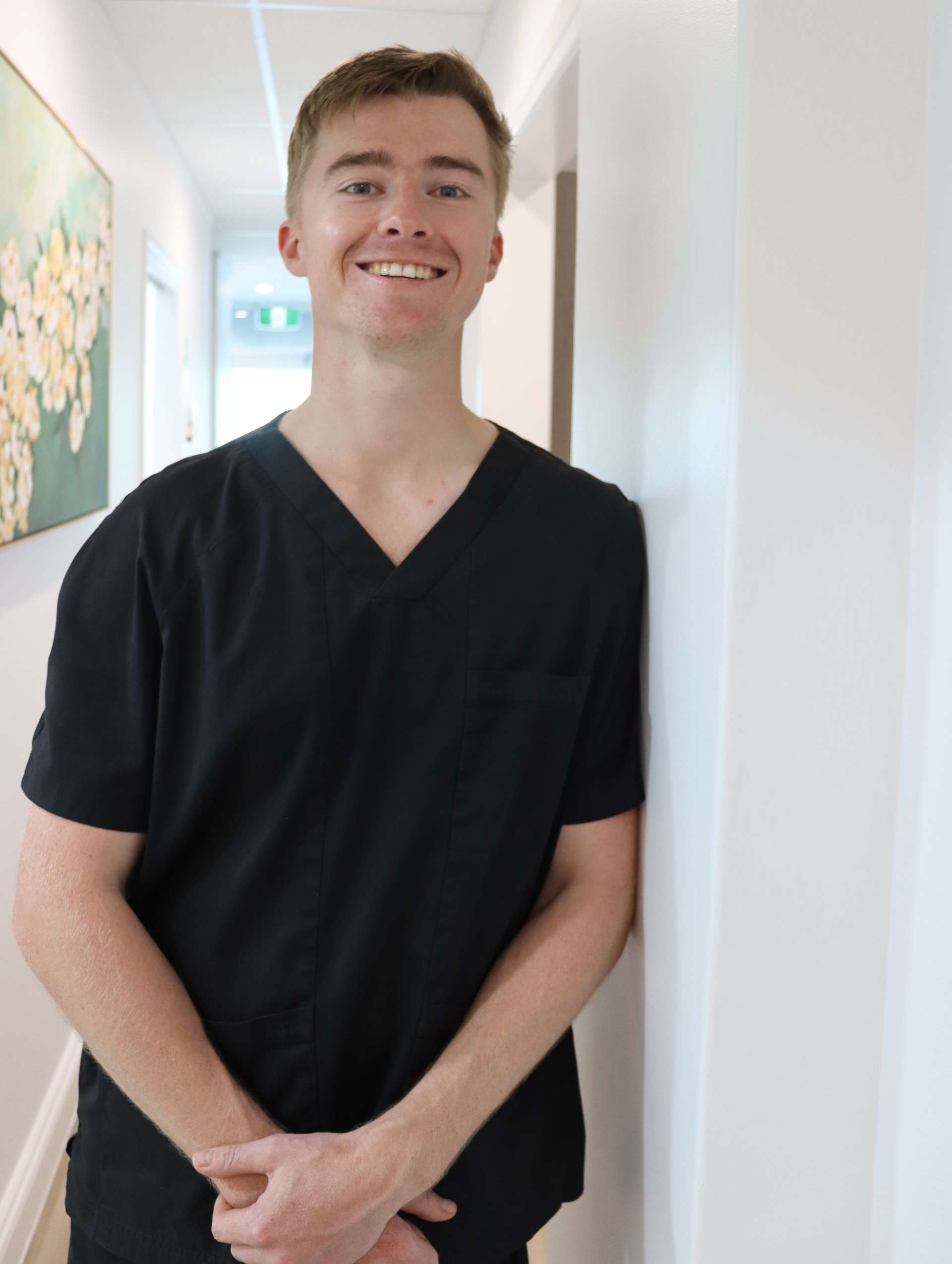 Person in a black shirt standing in a bright hallway, hands clasped, facing the camera. — Coronation House Dentist in Nambour, QLD