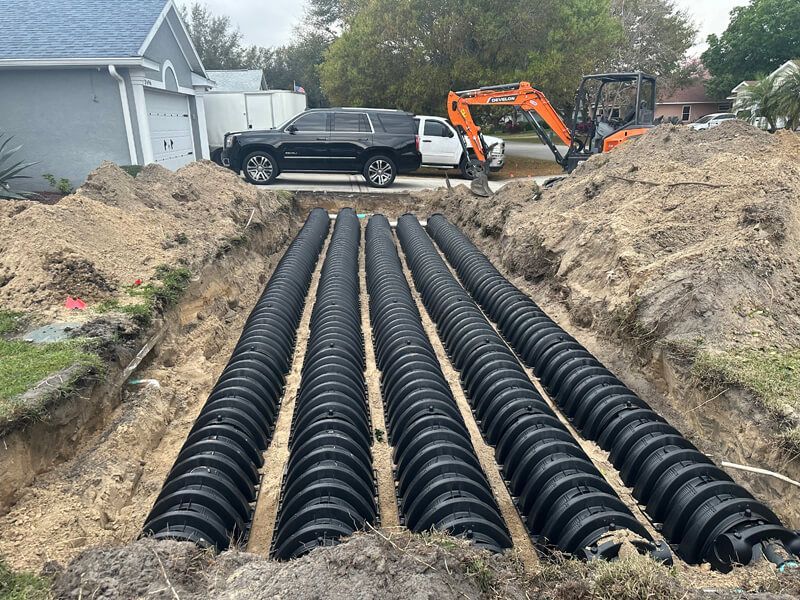 A construction site showing four parallel rows of black plastic septic drain field chambers laid in a trench.